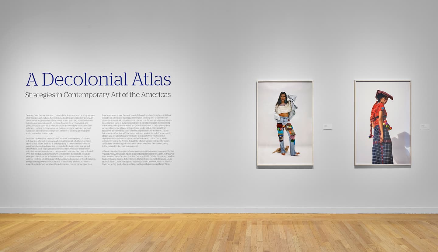 Image of a white gallery wall with the title and description of the exhibition on the left and two portraits on the right.