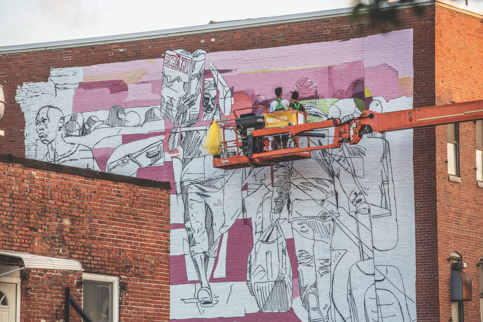 An artist paints a mural from the perch of a forklift.