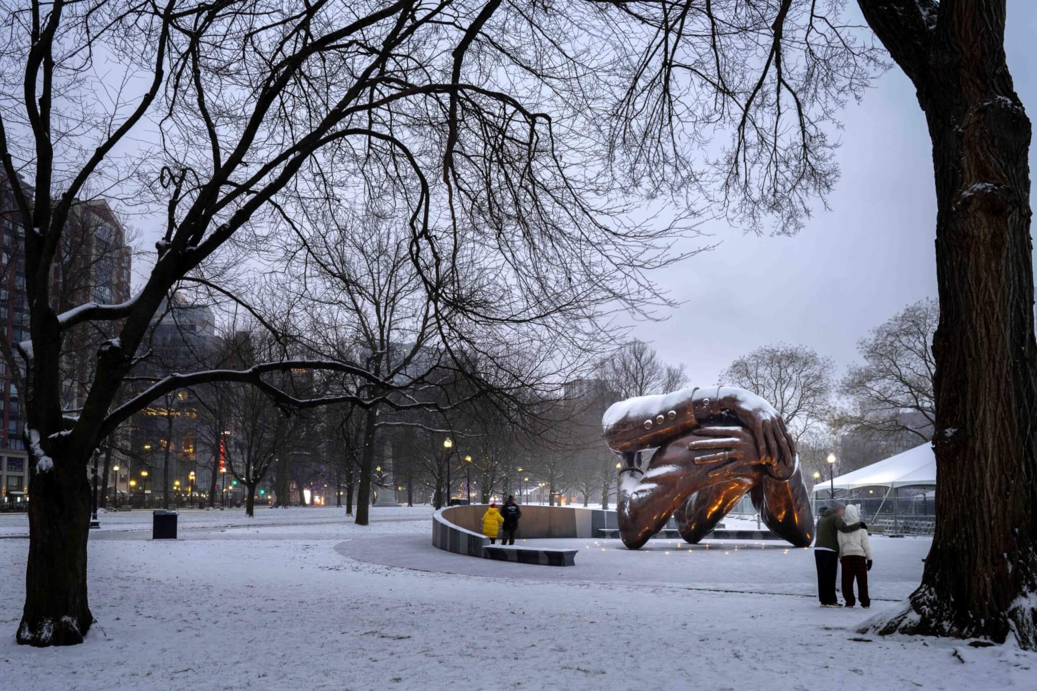 The Embrace sculpture, designed by Hank Willis Thomas, on a snowy day, found between bare trees.