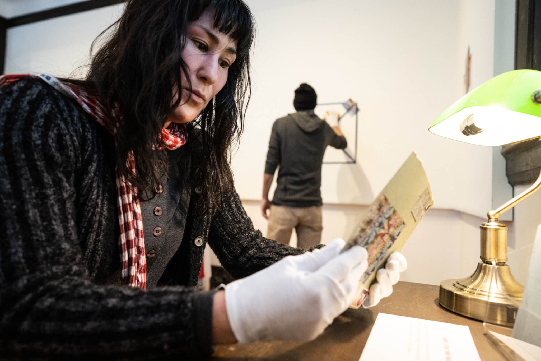 Mitsuko Brooks holds a letter, peering at it intently, while wearing white gloves.